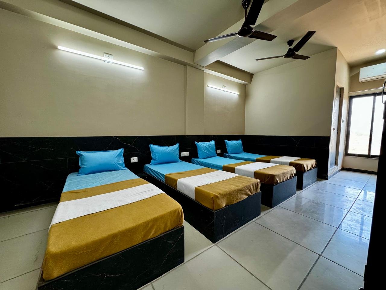 Quintuple sharing room with five beds, modern yellow hostel building visible outside window